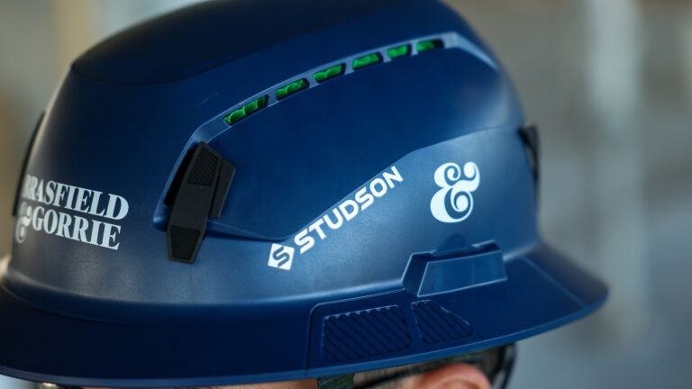Close-up of a blue Studson safety helmet with Brasfield & Gorrie branding, showing its ventilation slits and part of the wearer’s head.