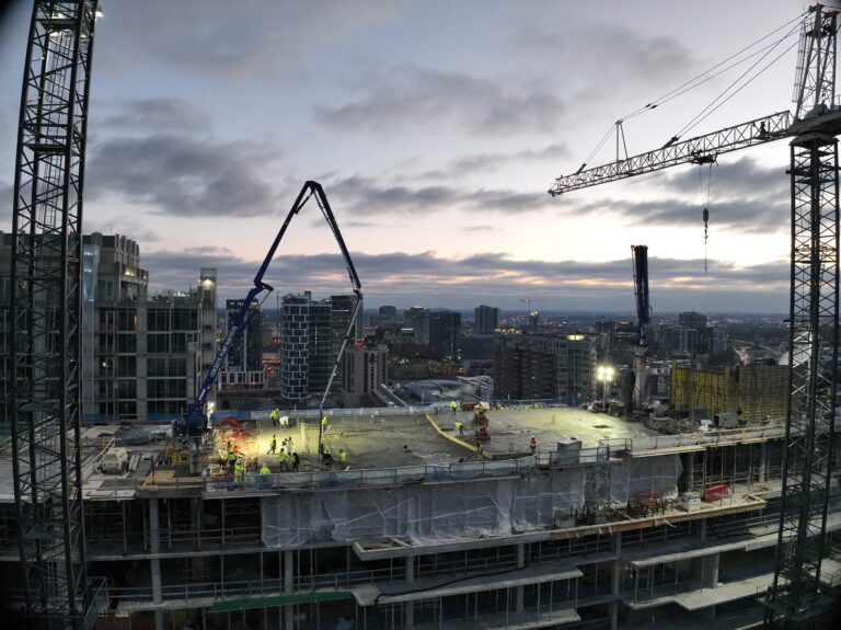 Obra de un rascacielos al atardecer, con grúas y trabajadores en la torre residencial 1740 Division, de Brasfield & Gorrie, aún en fase de construcción; al fondo, los edificios de la ciudad de Nashville y un cielo nublado.