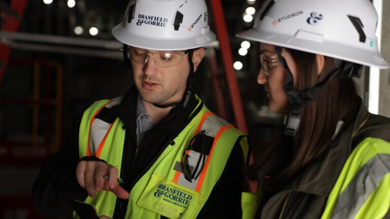 Two construction workers in safety gear and hard hats discuss a project at a work site, with one pointing out of view—highlighting the opportunities available through Brasfield and Gorrie Georgia careers.