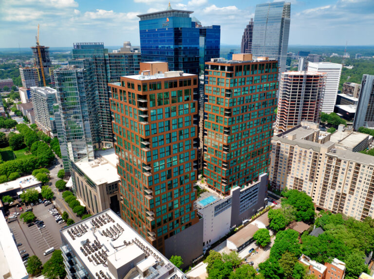 Aerial view of two tall, brown modern apartment buildings built by Brasfield and Gorrie, surrounded by other high-rise structures in a cityscape with trees and blue sky.
