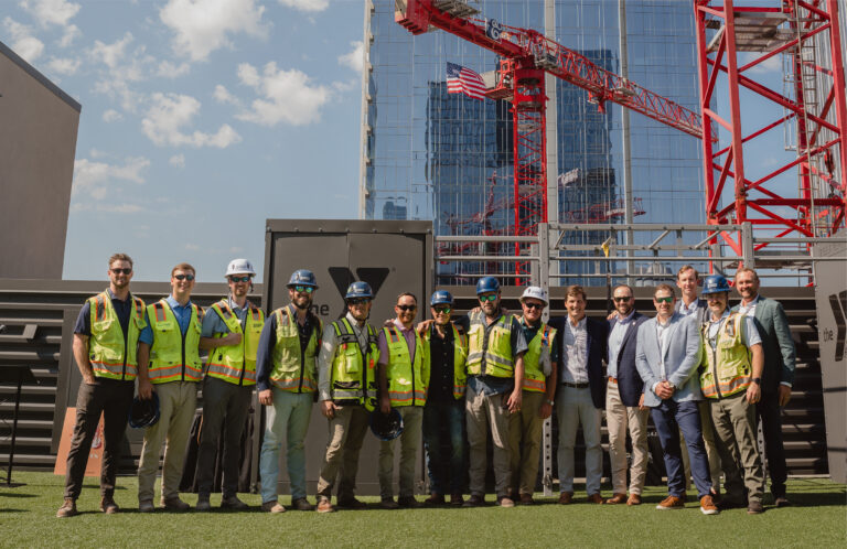 A group of people in safety vests and helmets stand in front of a Brasfield and Gorrie construction site, with cranes and tall buildings in the background.