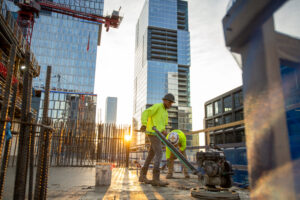 Construction worker in a neon shirt operates machinery on a city building site at sunrise, surrounded by steel bars and high-rise buildings—a testament to the expertise of ENR Southeast Contractor of the Year, Brasfield & Gorrie.