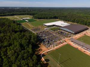 Aerial view of a large sports complex and U.S. Soccer Training Center with multiple soccer fields, parking lots, and buildings, surrounded by trees and forested areas.