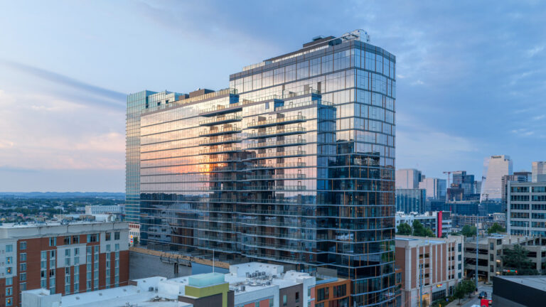 High-rise glass apartment building at Marston Music Row standing in a city skyline at sunset.