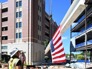 Un obrero de la construcción observa cómo una grúa levanta una viga de acero envuelta en una bandera estadounidense en una obra de Brasfield &amp; Gorrie en el centro de Spartanburg.
