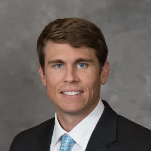 Headshot of a smiling man wearing a dark suit, white shirt, and blue patterned tie.