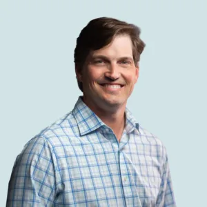 A smiling man wearing a light blue plaid button-down shirt.