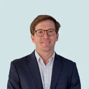 Un hombre que lleva gafas, una camisa estampada abotonada y una chaqueta azul marino.