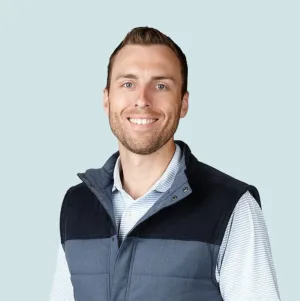Alec Brauning smiles while wearing a blue-and-white striped polo shirt under a two-toned navy and slate-blue quilted vest.