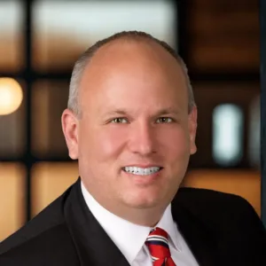 Brian Murray, a middle-aged man in a dark suit, white shirt, and red-and-navy striped tie.