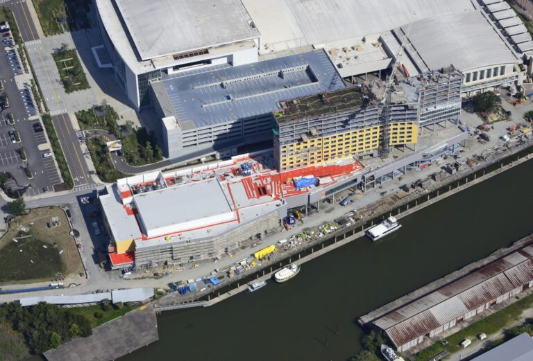 Aerial view of the Signia by Hilton Savannah construction site along a waterfront, featuring a parking garage and several boats docked nearby.