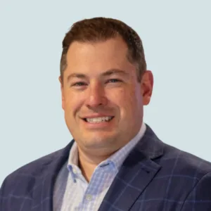 Headshot of a smiling man wearing a blue plaid sport coat and a light blue checked button-down shirt.