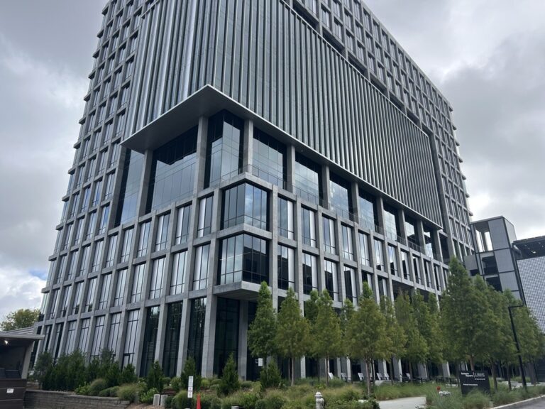 Un moderno edificio de oficinas de varios pisos, construido en cristal y hormigón, visto desde el nivel de la calle.