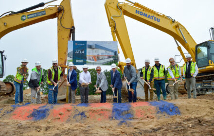 A group of contruction workers break ground in front of two pieces of yellow heavy machinery