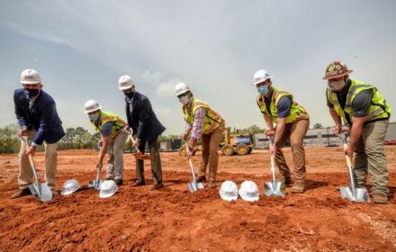 Five men in construction personal protective equipment break ground on a jobsite