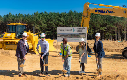 A group of five people in hard hats pose with shovels in front of a piece of construction equipment