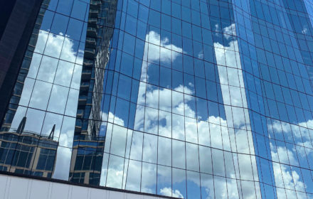A glass skyscraper with clouds reflected in its windows