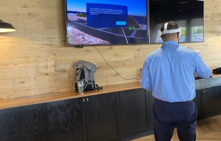 A man wearing a virtual-reality headset with a safety simulation shown on a television screen